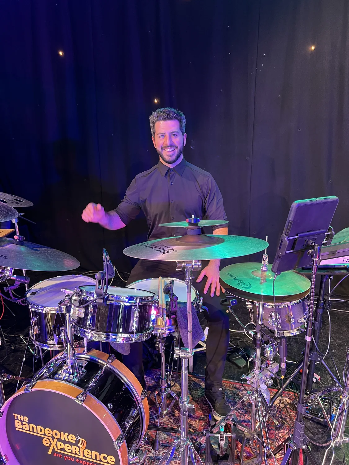 Oscar smiling behind an acoustic drum kit under coloured stage lighting